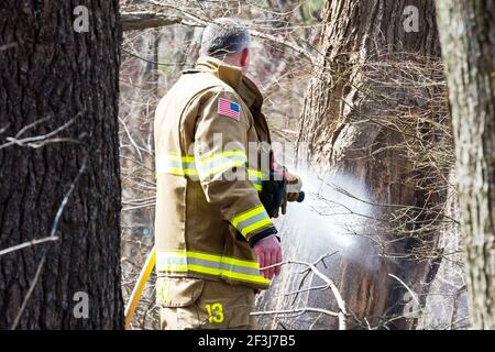 Un pompier pulvérise de l'eau pour contrôler un feu de broussailles. Banque D'Images