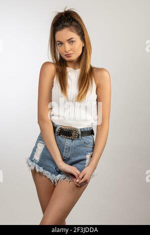 style de vie tourné d'un beau modèle italien étudiant, très mignon en short jeans et t-shirt blanc, posant sur blanc Banque D'Images