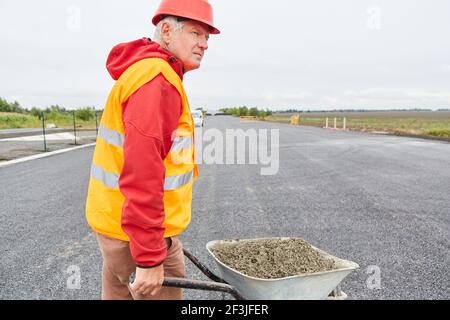 Les travailleurs sur le chantier pour réhabiliter le contournement avec une brouette pleine de béton Banque D'Images