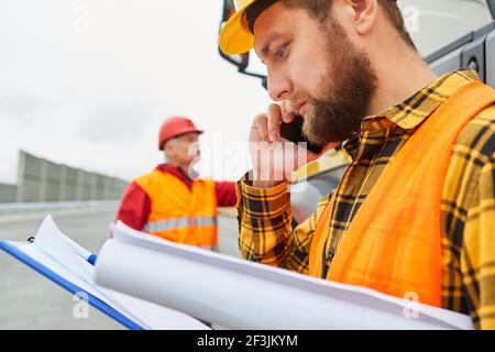 Travailleur de la construction avec des documents sur le téléphone avec téléphone portable sur le chantier de construction de la route Banque D'Images