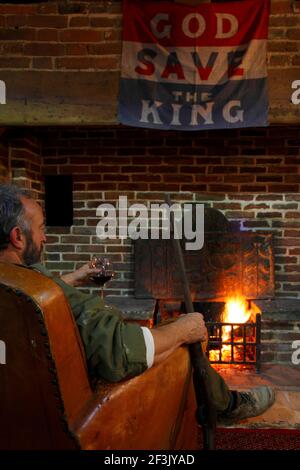 Un homme vu de derrière, assis avec un verre de vin rouge et une carabine devant un feu de pub ardu | | Concepteur : Richard Brett / nous aimons aujourd'hui Banque D'Images