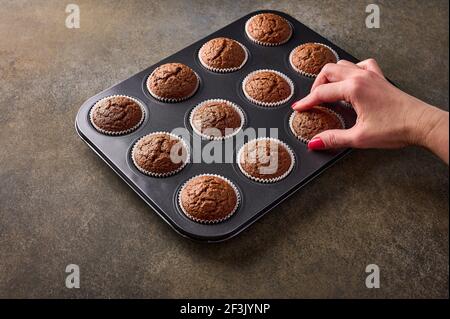 Main de femme avec une manucure tire un cupcake au chocolat de la pâtisserie sur fond de bois, gros plan Banque D'Images