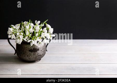 Bouquet de gouttes de neige blanches Galanthus nivalis en pot rétro vintage sur fond sombre avec espace de copie. Banque D'Images