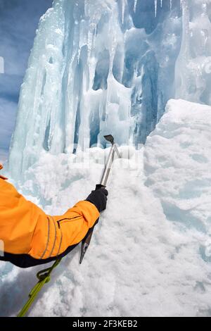 Femme grimpeur avec glace hache en veste orange près de la cascade gelée dans les montagnes de près à Almaty, Kazakhstan Banque D'Images