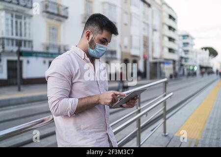 Un homme espagnol dans un masque de protection défilant sur une tablette; un homme occupé posant à l'extérieur Banque D'Images