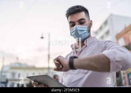 Un jeune homme espagnol portant un masque de protection tient une tablette et la vérification de l'heure Banque D'Images