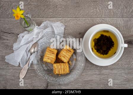 Composition du gâteau Napoléon, tasse de thé vert et fleur de jonquille. Gros plan, vue de dessus. Banque D'Images