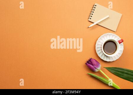 Carnet, crayon, tasse de café, fleur de tulipe sur fond orange. Lieu de travail et d'étude. plan d'examen, vue de dessus, espace de copie Banque D'Images