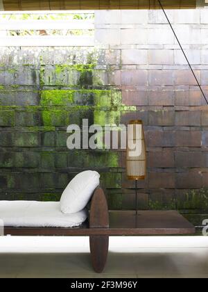 Lampe de table sur un siège moderne en bois à côté d'un mur de briques partiellement recouvert de mousse. Banque D'Images