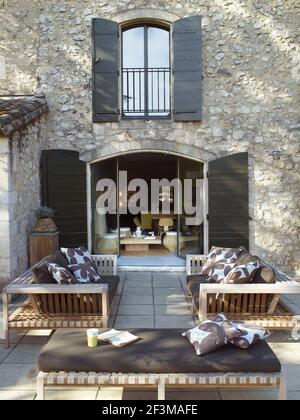 Deux canapés et une chaise longue sur le patio à côté des portes-fenêtres avec des volets en bois menant à la villa française. Banque D'Images