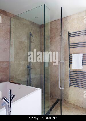 Douche avec mur en verre et porte à côté de la baignoire et porte de serviettes dans la salle de bains de la maison résidentielle, Royaume-Uni. Banque D'Images