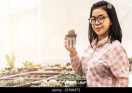 Authentique femme asiatique souriante tenant cactus dans un pot en plastique de plante dans la boutique de cactus. Concept de la maison du jardin intérieur. Banque D'Images