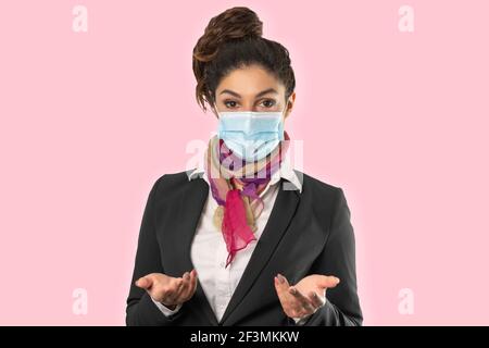 Un beau gardien de vol avec masque chirurgical, foulard multicolore et veste noire. Sujet sur fond rose. Photo parfaite pour les femmes au travail, pa Banque D'Images