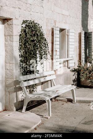 banc en bois peint en blanc à l'ombre devant une maison en pierre sous la fleur en été. Voyager Croatie. Vue sur la rue Banque D'Images