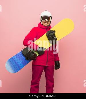 Snowboardeur mâle avec équipement de ski dans une combinaison de ski lumineuse isolée sur fond rose Banque D'Images