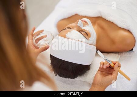 Esthéticienne couvrant la peau du visage de la femme avec un masque hydratant pendant les soins de la peau procédure Banque D'Images