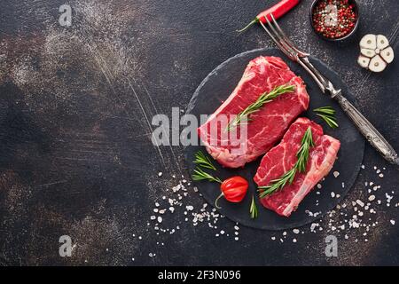 Deux steaks crus New York au romarin et aux épices. Plan de travail à plat sur la barre de coupe en pierre noire.