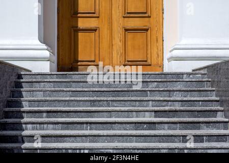 escalier en granit gris escalier à l'entrée de la porte en bois marron avec murs de façade blancs illuminés par la lumière du soleil bâtiment architectural, personne. Banque D'Images