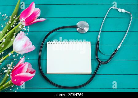 Tulipes roses et stéthoscope avec bloc-notes en spirale avec texte « Happy Doctors Day ». plan d'examen en plan, Banque D'Images