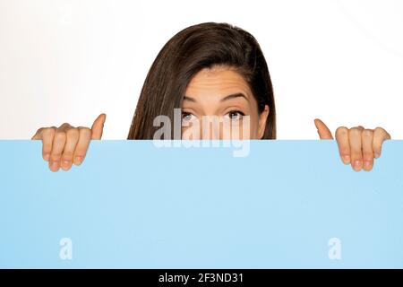 jeune belle femme qui se cache derrière un tableau bleu vide arrière-plan blanc Banque D'Images