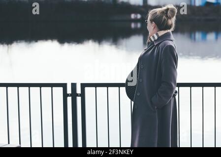 vue latérale d'une femme blonde très enceinte qui regarde la rivière Banque D'Images