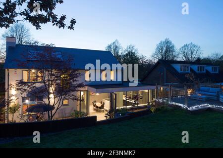 Arrière de la maison avec sièges extérieurs et portes doubles ouvertes au crépuscule | architecte : McAfee Design | Banque D'Images