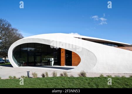 Une structure externe courbée blanche et spectaculaire autour d'un bâtiment qui offre des espaces de traitement et sociaux pour les patients atteints de cancer, dans le domaine d'un hôpital. Banque D'Images