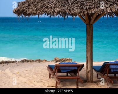 Parasol de plage de palmiers et deux lits à tréteaux vides sur la plage de sable de l'océan Turquoise sous le ciel bleu de Zanzibar. Arrière-plan des vacances d'été Banque D'Images