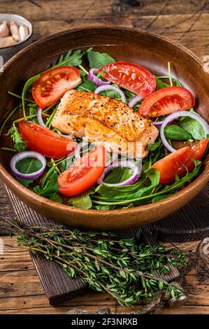 Salade de steak de saumon avec feuilles vertes, arugula, avocat et tomate dans une assiette en bois. Arrière-plan en bois. Vue de dessus Banque D'Images