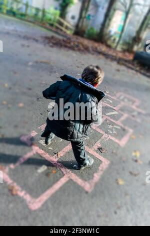 Enfant de l'école primaire jouant le hopscotch dans un terrain de jeu de l'école pendant leur pause des leçons de classe. Banque D'Images