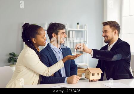 Un couple multiethnique millénaire souriant prend la clé de l'agent immobilier Banque D'Images