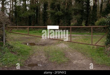 Une porte en métal rouillé fermée avec un panneau blanc, à travers un champ de fermiers. Banque D'Images