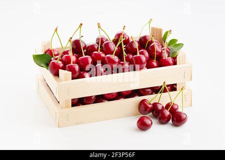 Cerises douces fraîches et mûres dans une petite caisse en bois sur fond blanc. Banque D'Images
