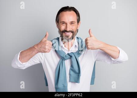 Photo de bonne humeur positive âge homme porter chemise blanche épaules du chandail montrant les pouces vers le haut, fond gris isolé Banque D'Images