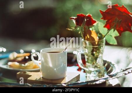 Brunch en plein air avec gros plan d'une tasse de café expresso sur un plateau argenté vintage et roses, fond bokeh Banque D'Images