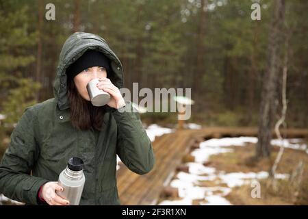 Les femmes boit la boisson de la tasse et tient le termos dans l'autre main. Repos prenant une pause pendant la randonnée. Banque D'Images