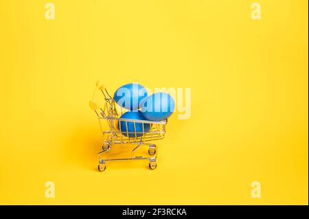 Trois gros œufs bleus dans un chariot de supermarché sur fond jaune vif. Concept d'achat de produits sans quitter la maison Banque D'Images