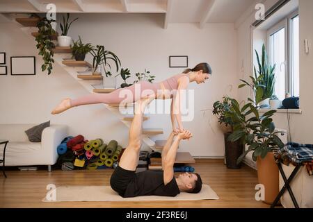 Jeune couple pratiquant l'acro yoga ensemble à la maison dans un intérieur moderne. Passe-temps, ensemble, mode de vie sain Banque D'Images