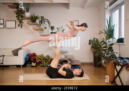 Jeune couple pratiquant l'acro yoga ensemble à la maison dans un intérieur moderne. Passe-temps, ensemble, mode de vie sain Banque D'Images