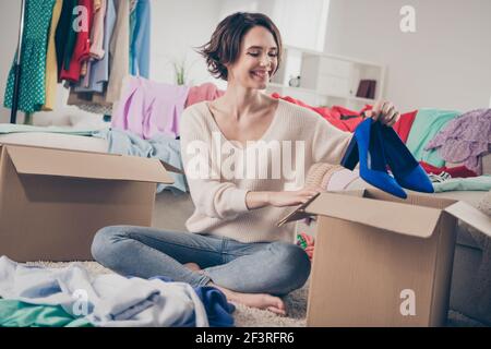 Pleine photo de jolie fille positive bras tenir la mise chaussures dans une boîte sourire en dents de souris assis sur le tapis de sol le week-end intérieur Banque D'Images