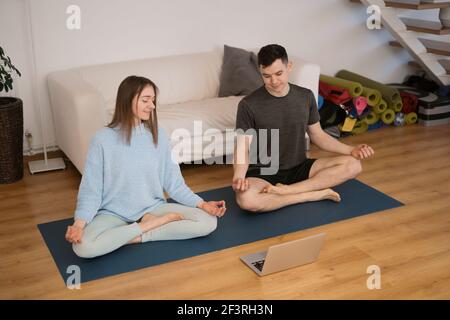 Beau couple pratiquant le yoga ensemble à la maison à l'aide d'un ordinateur portable suivre des cours de yoga en ligne Banque D'Images