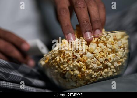 Bon goût. Gros plan sur une main masculine prenant du pop-corn dans un bol Banque D'Images