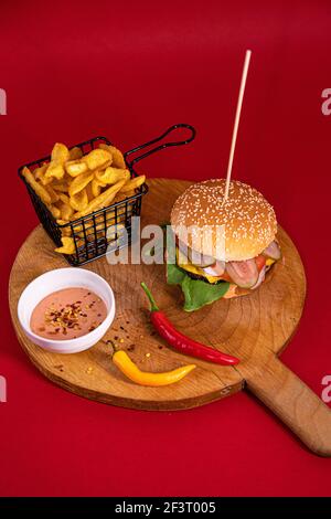 A big burger, french fries, Fry sauce and two chili peppersserved on a wooden board Stock Photo