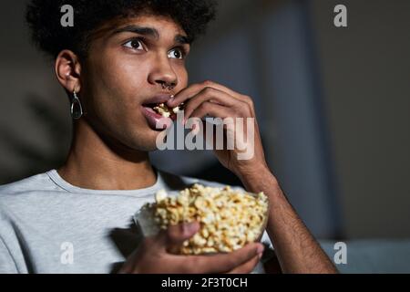 Gros plan sur un jeune homme qui mange du pop-corn tout en regardant cinéma à la maison Banque D'Images