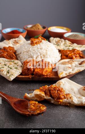 Image en angle d'un mélange gastronomique de plats indiens, y compris le riz, le naan, le tikka masala, le poulet au beurre et le curry. Les épices et les herbes sont visibles en flou Banque D'Images