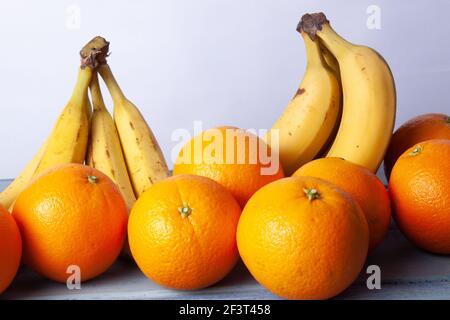 Vue sur les oranges et les bananes alignées sur un gris tableau sur fond blanc Banque D'Images