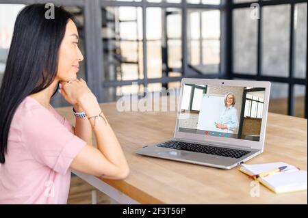 Femme asiatique attentive utilisant l'application pour étudier en ligne via ordinateur portable, suivre un cours virtuel, écouter activement le conférencier, étudier à la maison, vieille enseignante expliquant le matériel sur tableau blanc Banque D'Images