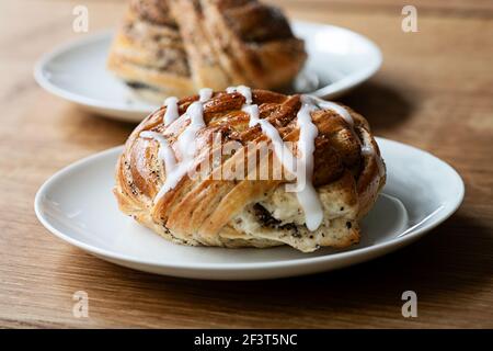 Un pain de cardamon suédois (également appelé rouleau de cardamon) sur une assiette. En arrière-plan, hors foyer, se trouve une assiette avec un petit pain à la cannelle avec glaçage. Banque D'Images