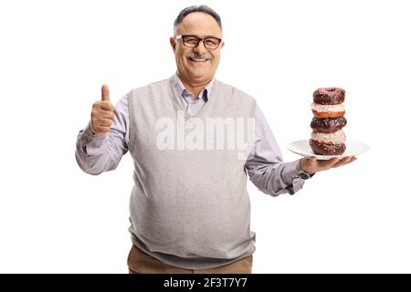 Homme mûr souriant tenant une assiette de beignets et gesturant un signe de pouce vers le haut isolé sur fond blanc Banque D'Images