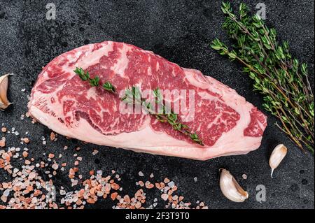 Steak de stripine brut sur une table de boucher avec sel et thym. Arrière-plan noir. Vue de dessus Banque D'Images
